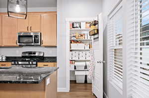 Kitchen featuring light brown cabinets, dark wood-type flooring, dark stone countertops, pendant lighting, and appliances with stainless steel finishes