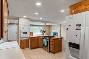 Kitchen featuring sink, light tile patterned floors, white appliances, a textured ceiling, and kitchen peninsula