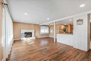 Unfurnished living room featuring a brick fireplace, dark hardwood / wood-style floors, and a textured ceiling