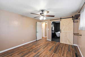 Primary bedroom with a barn door, ensuite bath, dark hardwood / wood-style flooring, a closet, and ceiling fan