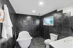 Primary bathroom featuring separate shower and tub, vanity, tile walls, and toilet