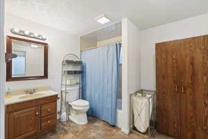 Full bathroom with vanity, shower / bath combination with curtain, a textured ceiling, and toilet