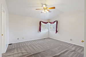 Carpeted spare room featuring ceiling fan and lofted ceiling