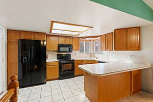 Kitchen featuring kitchen peninsula, a textured ceiling, sink, black appliances, and light tile patterned floors