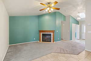 Unfurnished living room featuring light colored carpet, ceiling fan, lofted ceiling, and a tiled fireplace