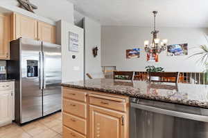 Kitchen featuring stainless steel appliances, vaulted ceiling, light tile patterned flooring, light brown cabinets, and decorative light fixtures