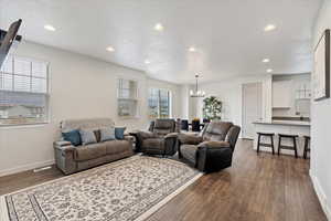 Living room with dark wood-type flooring, a textured ceiling, and an inviting chandelier