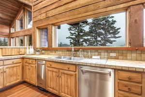 Kitchen featuring wooden ceiling, light hardwood / wood-style flooring, stainless steel dishwasher, tile countertops, and vaulted ceiling