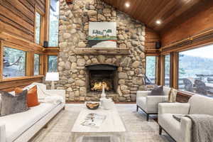 Living room with a stone fireplace, a wealth of natural light, hardwood / wood-style floors, and wood ceiling