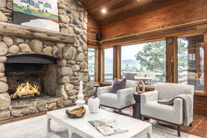 Living room featuring vaulted ceiling, wood ceiling, hardwood / wood-style floors, and a stone fireplace