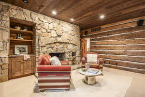 Living area featuring light carpet, a fireplace, wooden ceiling, and log walls