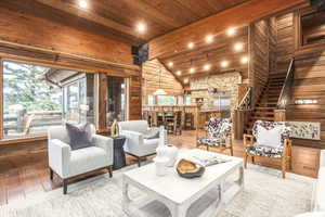 Living room with wooden ceiling, vaulted ceiling with beams, wood walls, and wood-type flooring