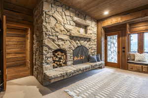 Unfurnished living room with a stone fireplace, wooden walls, and wood ceiling