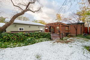 Snow covered back of property with a pergola and a deck