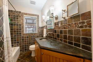 Full bathroom featuring vanity, toilet, shower / bath combo, and tile walls