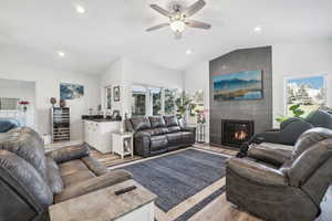 Living room featuring light hardwood / wood-style floors, ceiling fan, lofted ceiling, and a tiled fireplace