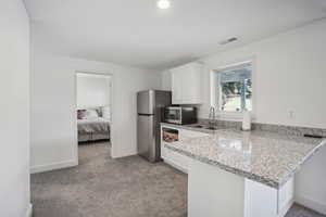 Kitchen with white cabinetry, sink, stainless steel appliances, and light colored carpet