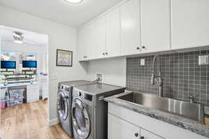 Laundry area with sink, washer and clothes dryer, cabinets, ceiling fan, and light wood-type flooring