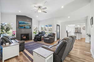 Living room with a tile fireplace, light hardwood / wood-style floors, ceiling fan, and lofted ceiling