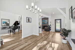 Entryway featuring ceiling fan with notable chandelier, hardwood / wood-style floors, a large fireplace, and lofted ceiling