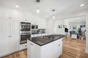 Kitchen with decorative backsplash, stainless steel appliances, decorative light fixtures, light hardwood / wood-style floors, and white cabinetry