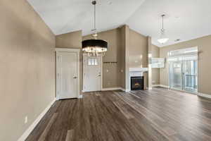 Unfurnished living room featuring high vaulted ceiling, a notable chandelier, and dark hardwood / wood-style flooring