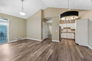 Interior space with dark wood-type flooring, hanging light fixtures, stainless steel fridge, decorative backsplash, and white cabinets