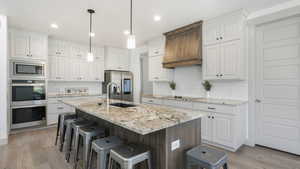 Kitchen with white cabinetry, tasteful backsplash, light hardwood / wood-style flooring, a kitchen island with sink, and appliances with stainless steel finishes