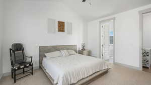 Carpeted bedroom with ceiling fan, lofted ceiling, and ensuite bathroom