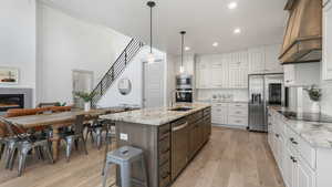 Kitchen featuring white cabinetry, a center island with sink, stainless steel appliances, and custom exhaust hood