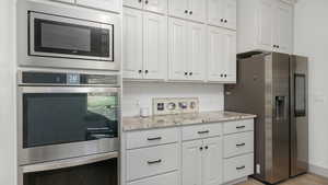 Kitchen featuring white cabinets, appliances with stainless steel finishes, backsplash, light wood-type flooring, and light stone countertops