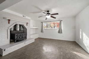 Unfurnished living room with a wood stove, ceiling fan, and a textured ceiling