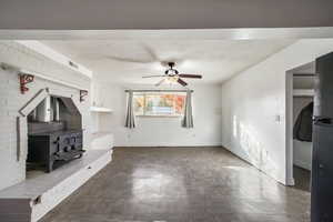 Unfurnished living room featuring a wood stove and ceiling fan