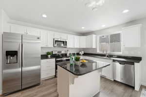 Kitchen featuring light lvp flooring, sink, white cabinets, a kitchen island, and stainless steel appliances