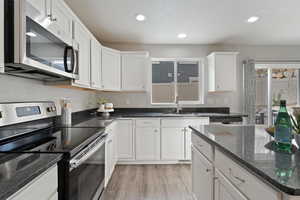 Kitchen with white cabinets, appliances with stainless steel finishes, light lvp flooring, and sink