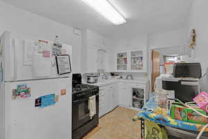 Kitchen featuring white cabinetry, white refrigerator, black range with gas cooktop, and a textured ceiling