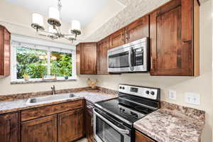 Kitchen with a chandelier, sink, light stone countertops, and stainless steel appliances