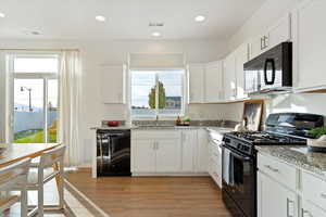 Kitchen with black appliances, white cabinetry, light hardwood / wood-style floors, and light stone counters