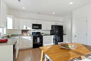 Kitchen with white cabinets, sink, black appliances, light wood-type flooring, and light stone counters