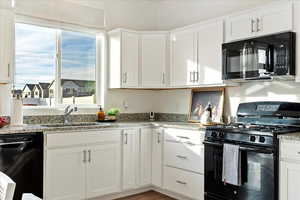 Kitchen with white cabinets, sink, light stone countertops, and black appliances