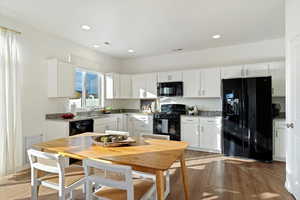 Kitchen featuring light hardwood / wood-style flooring, white cabinetry, sink, black appliances, and light stone counters