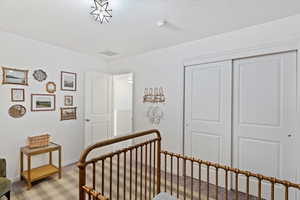 Bedroom featuring a closet, light colored carpet, a nursery area, and a textured ceiling