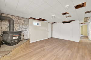 Basement with light hardwood / wood-style flooring and a wood stove