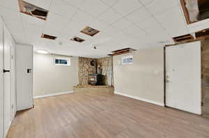 Basement featuring a paneled ceiling, light hardwood / wood-style flooring, a wood stove, and a healthy amount of sunlight