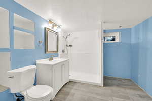 Bathroom with a shower, a textured ceiling, vanity, and toilet