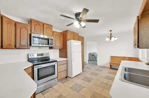 Kitchen with appliances with stainless steel finishes, ceiling fan with notable chandelier, decorative light fixtures, and sink