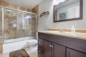 Full bathroom featuring tile patterned floors, vanity, a textured ceiling, enclosed tub / shower combo, and toilet