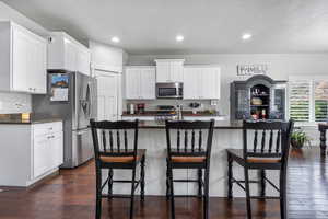 Kitchen with white cabinets, appliances with stainless steel finishes, a kitchen island with sink, and dark stone countertops