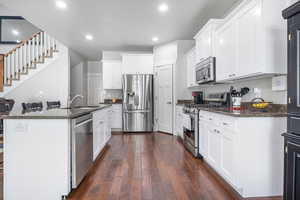 Kitchen featuring stainless steel appliances, dark wood-type flooring, sink, a center island with sink, and white cabinets