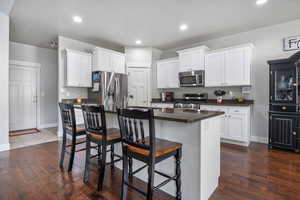 Kitchen with white cabinetry, an island with sink, dark wood-type flooring, and appliances with stainless steel finishes